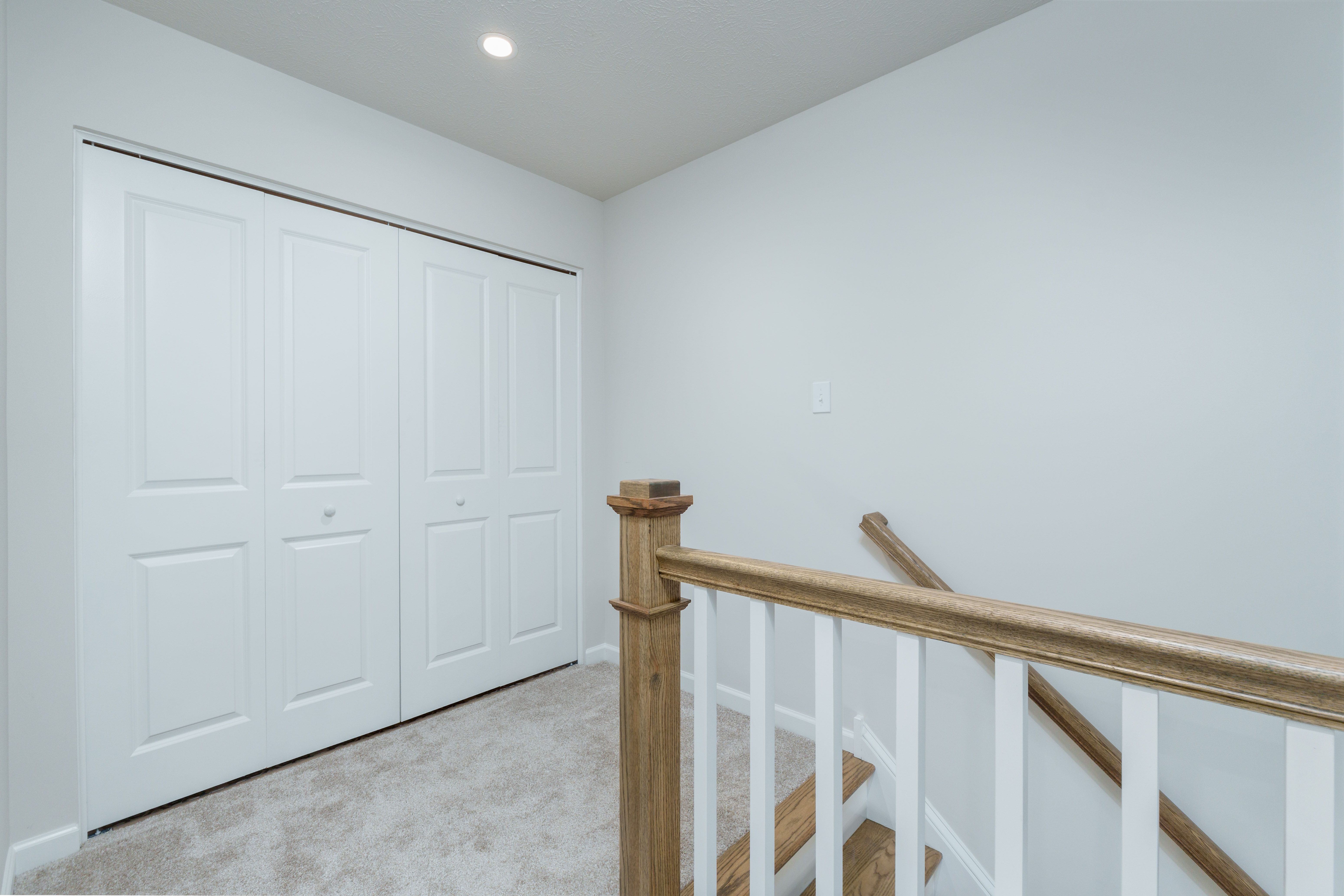 Upper hallway with carpeted floor, wood railing, and white double doors leading to laundry area.