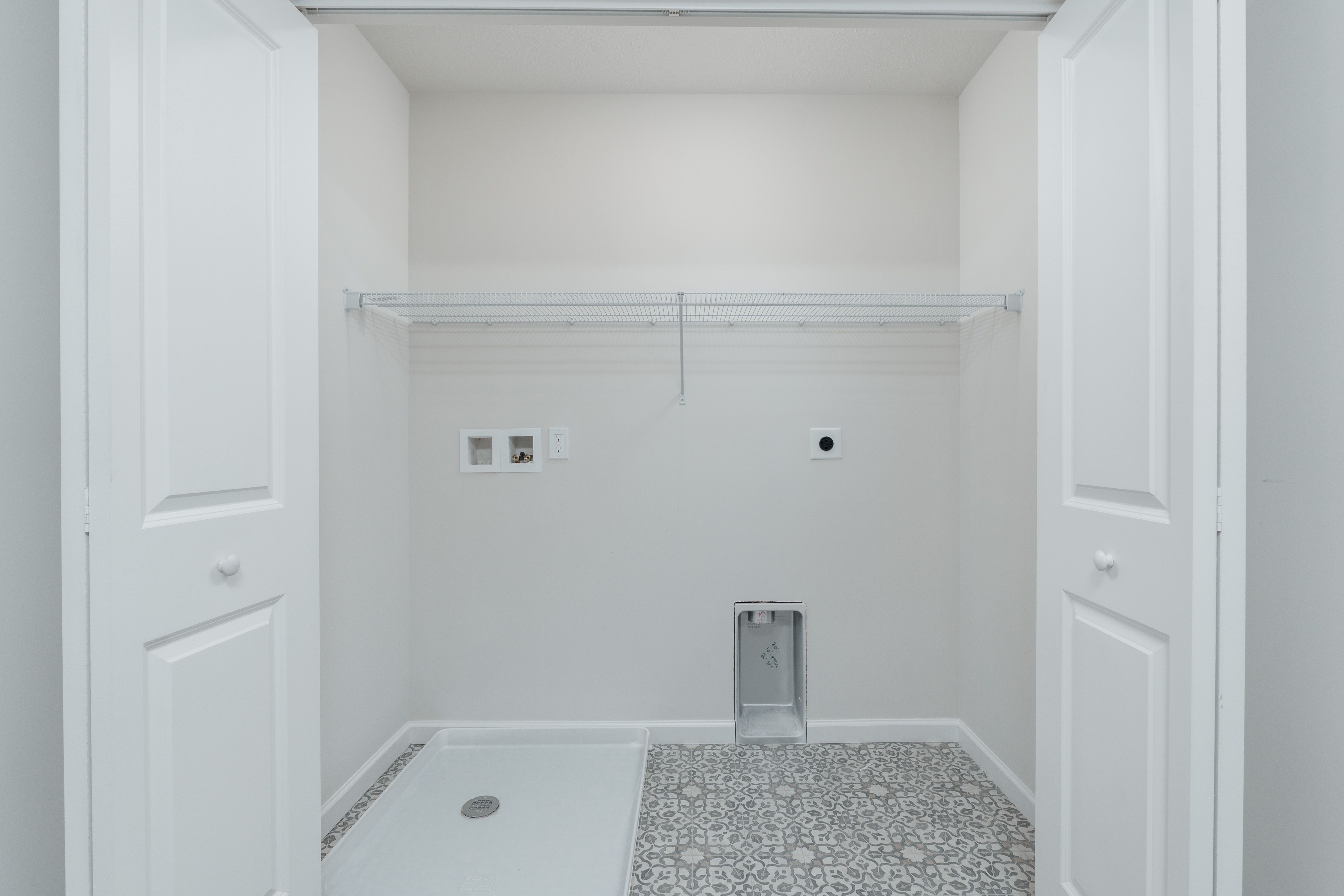 Laundry room with patterned tile floor, washer/dryer hookups, and white wire shelf inside folding doors.