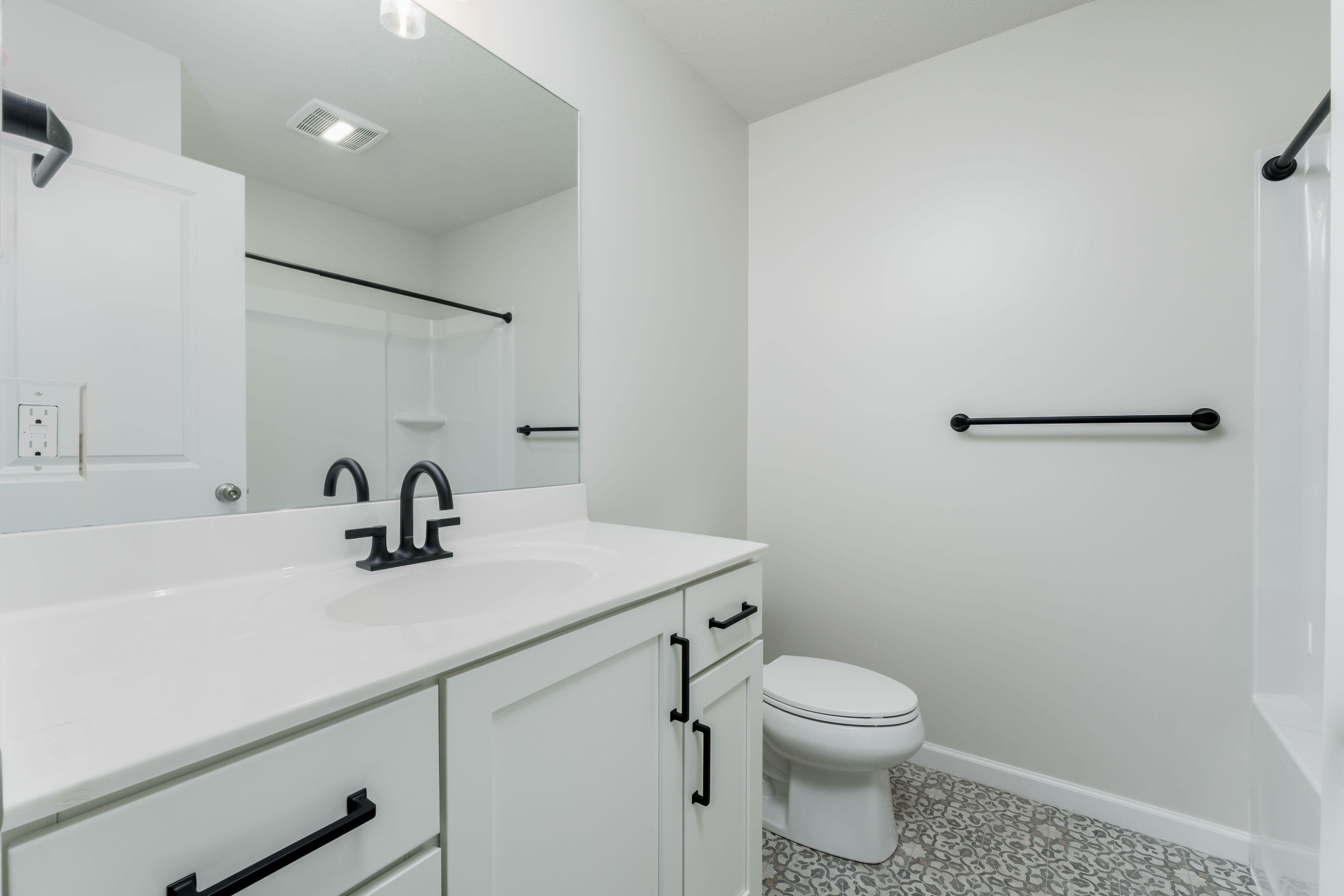 Bright bathroom with white vanity, matte black fixtures, large mirror, and patterned tile flooring.