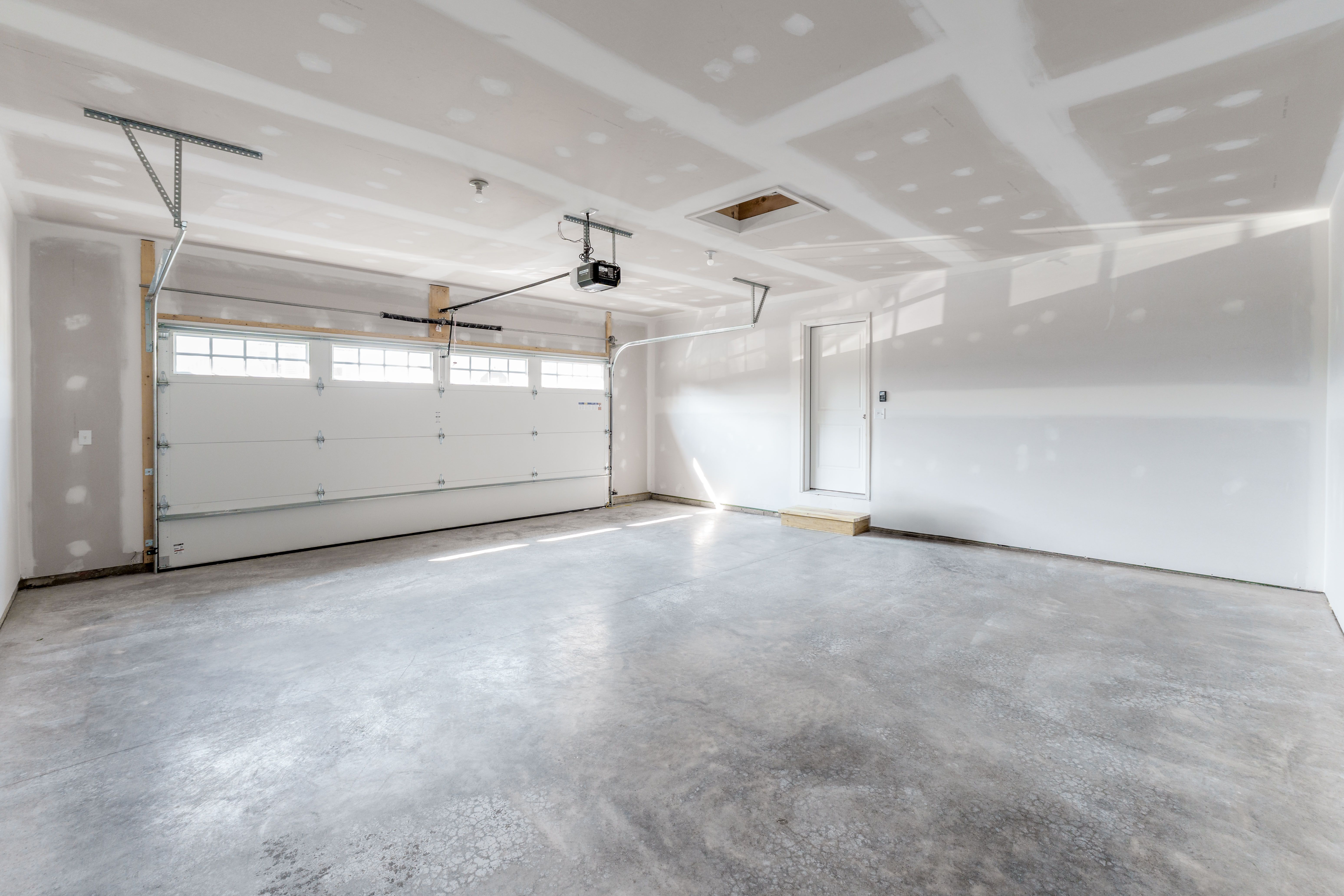 Unfinished two-car garage with concrete floor, white garage door with windows, and drywall ceiling.