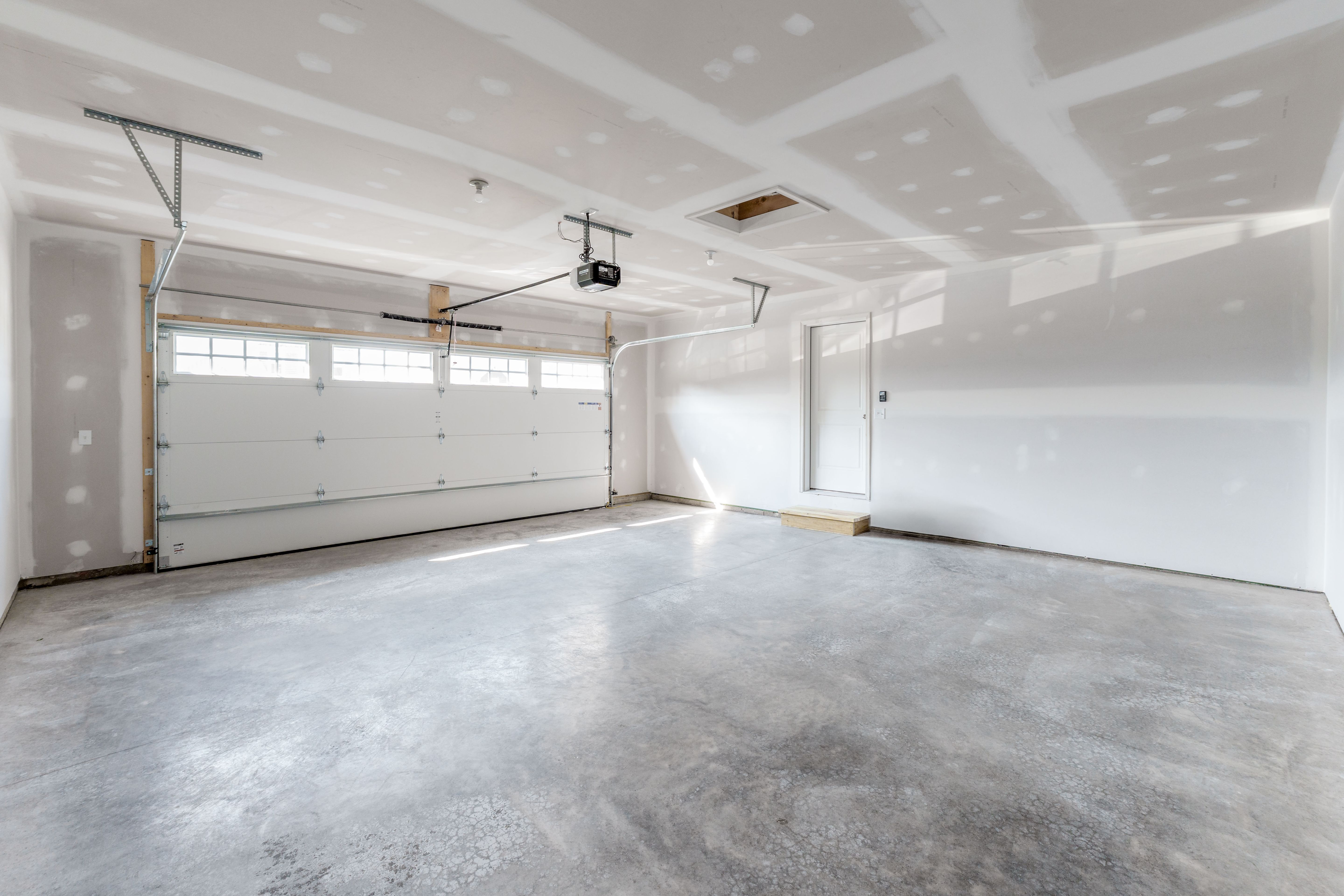 Unfinished two-car garage with concrete floor, white garage door with windows, and drywall ceiling.