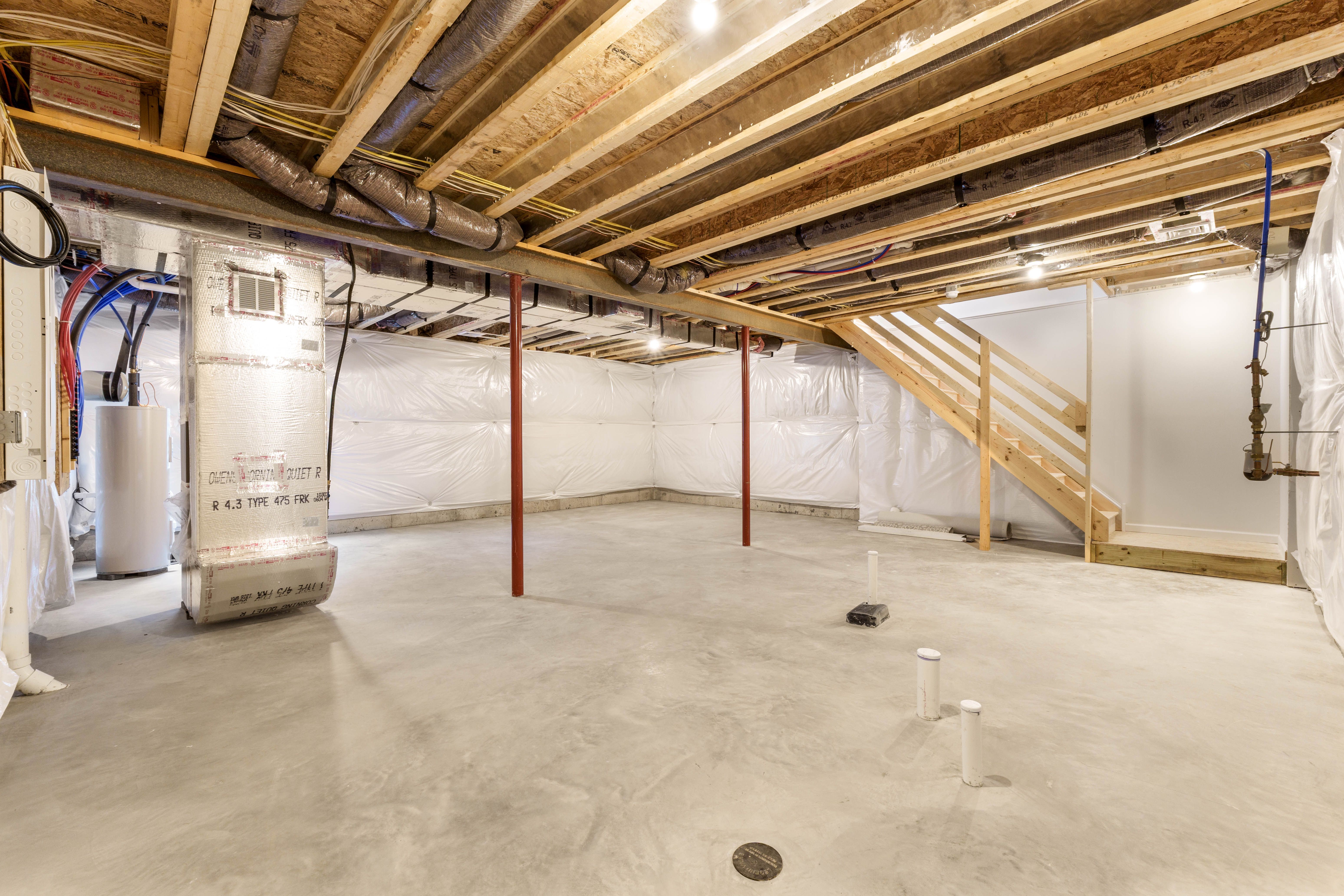 View of unfurnished basement with structural support beams, concrete floors, and open wood staircase to main level.