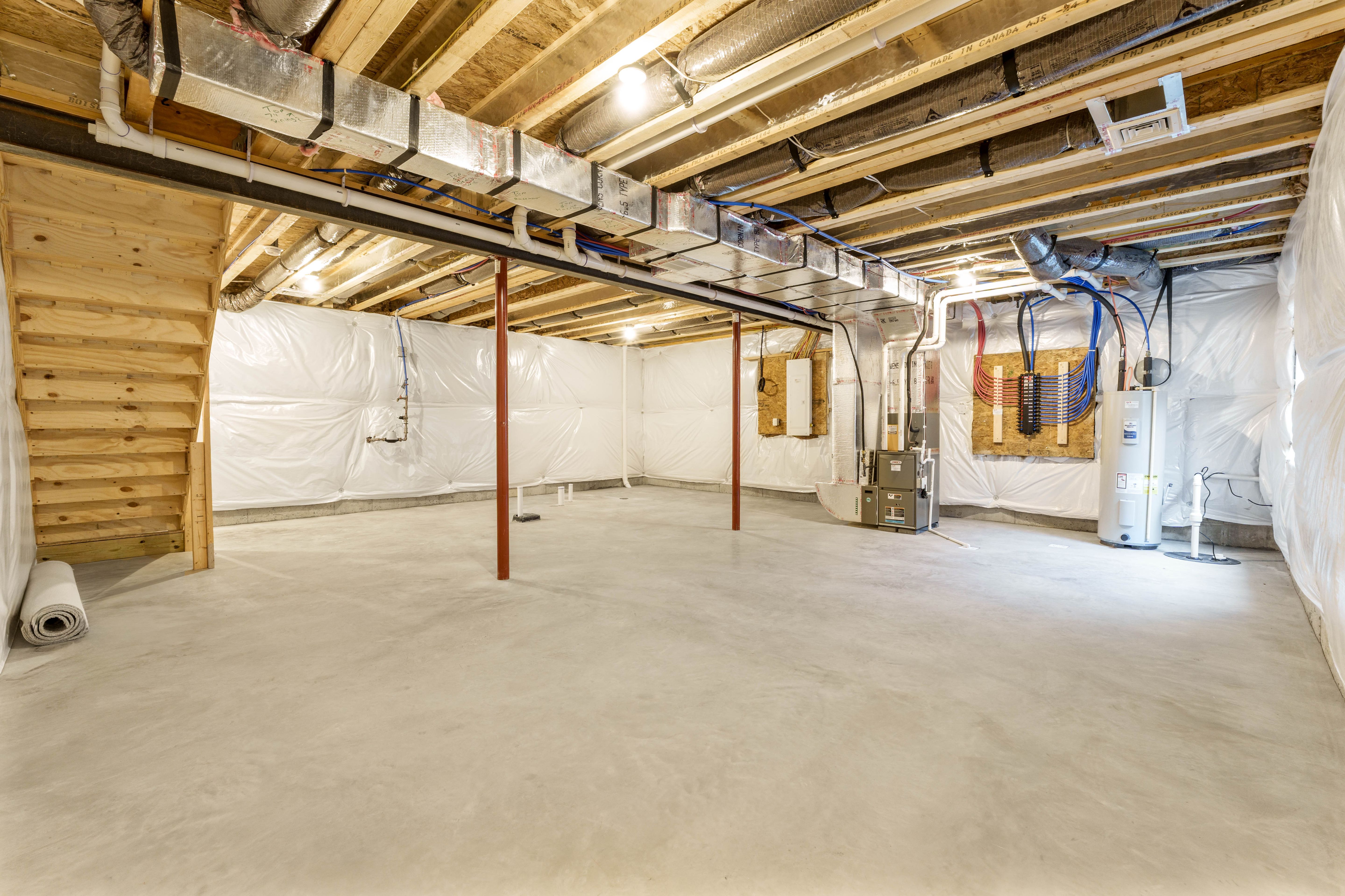 Wide view of an unfurnished basement featuring concrete floors, stairs, HVAC system, and wrapped insulated walls.