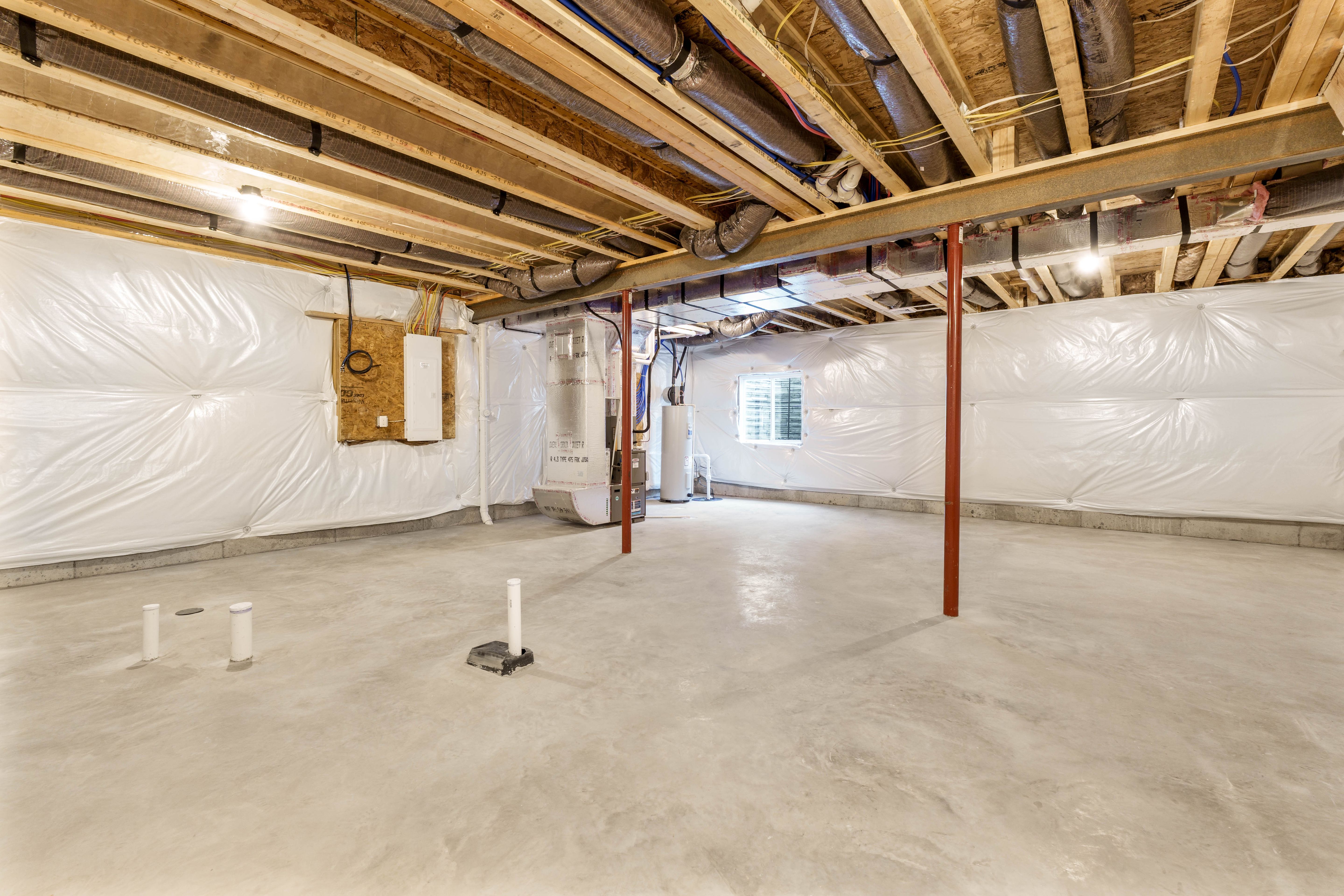Unfurnished basement with concrete floors, exposed ceiling beams, and visible HVAC ductwork and utility panels.