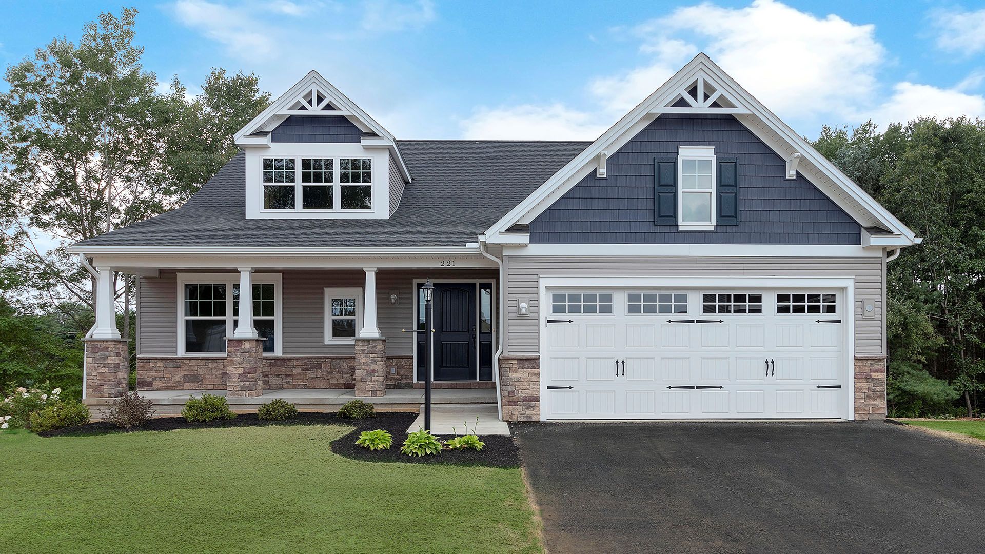 Front exterior of a charming home with blue and gray siding, stone accents, dormer windows, front porch, and landscaped yard.