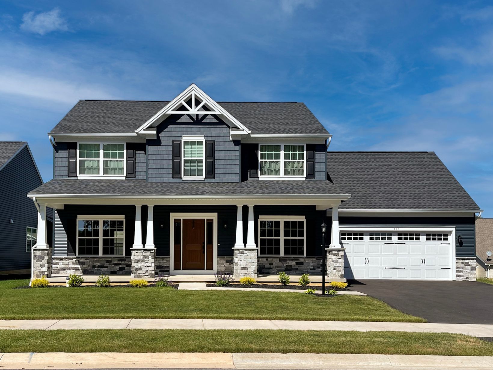 Exterior of a two-story home with dark blue siding, white trim, stone accents, covered porch, and attached garage.