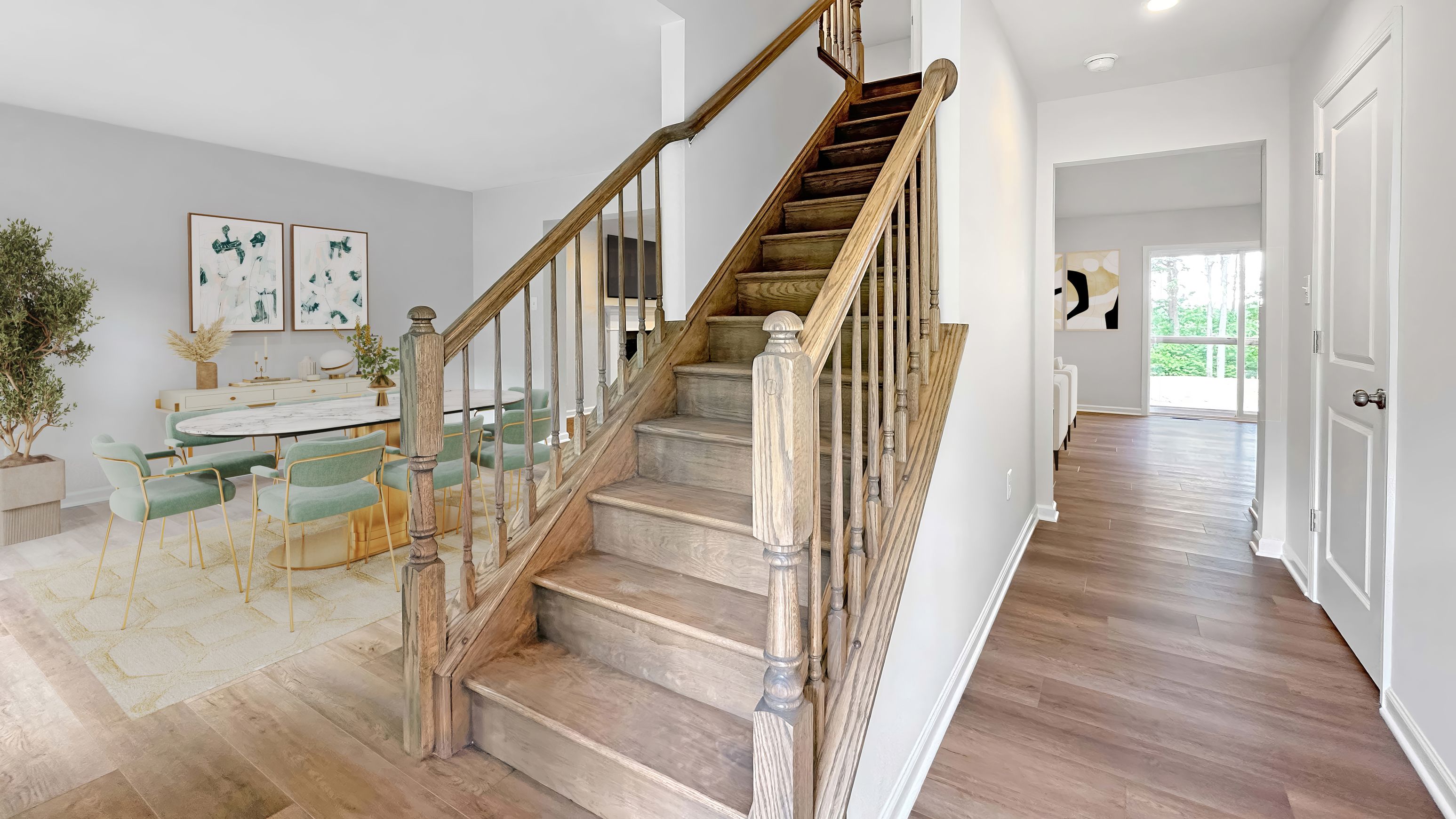 Staircase entryway with natural wood stairs adjacent to an open dining area featuring modern furnishings and artwork.