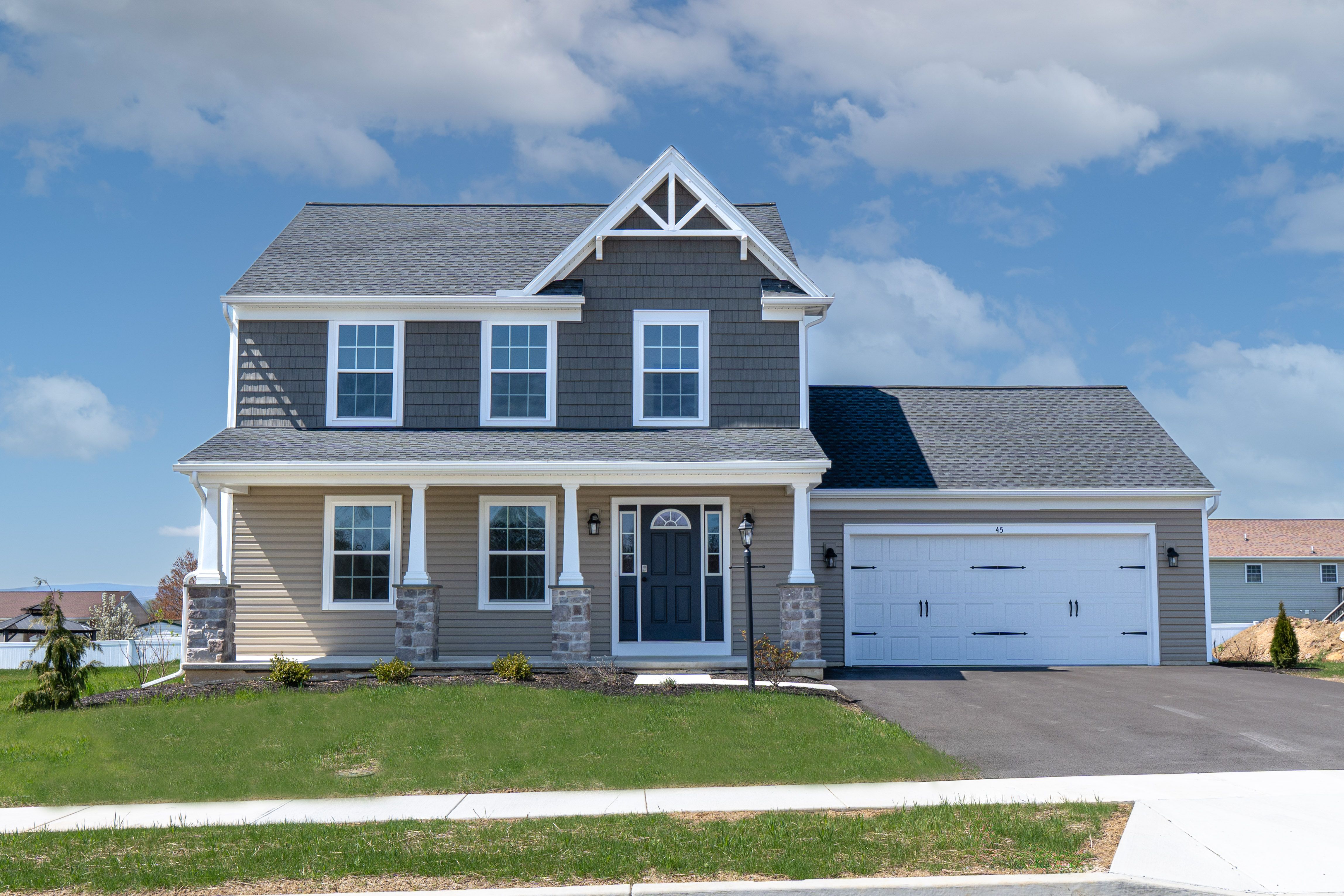 Full front-facing image of a two-story home featuring a covered front porch, stone columns, and a black front door, with a paved driveway leading to a white garage.