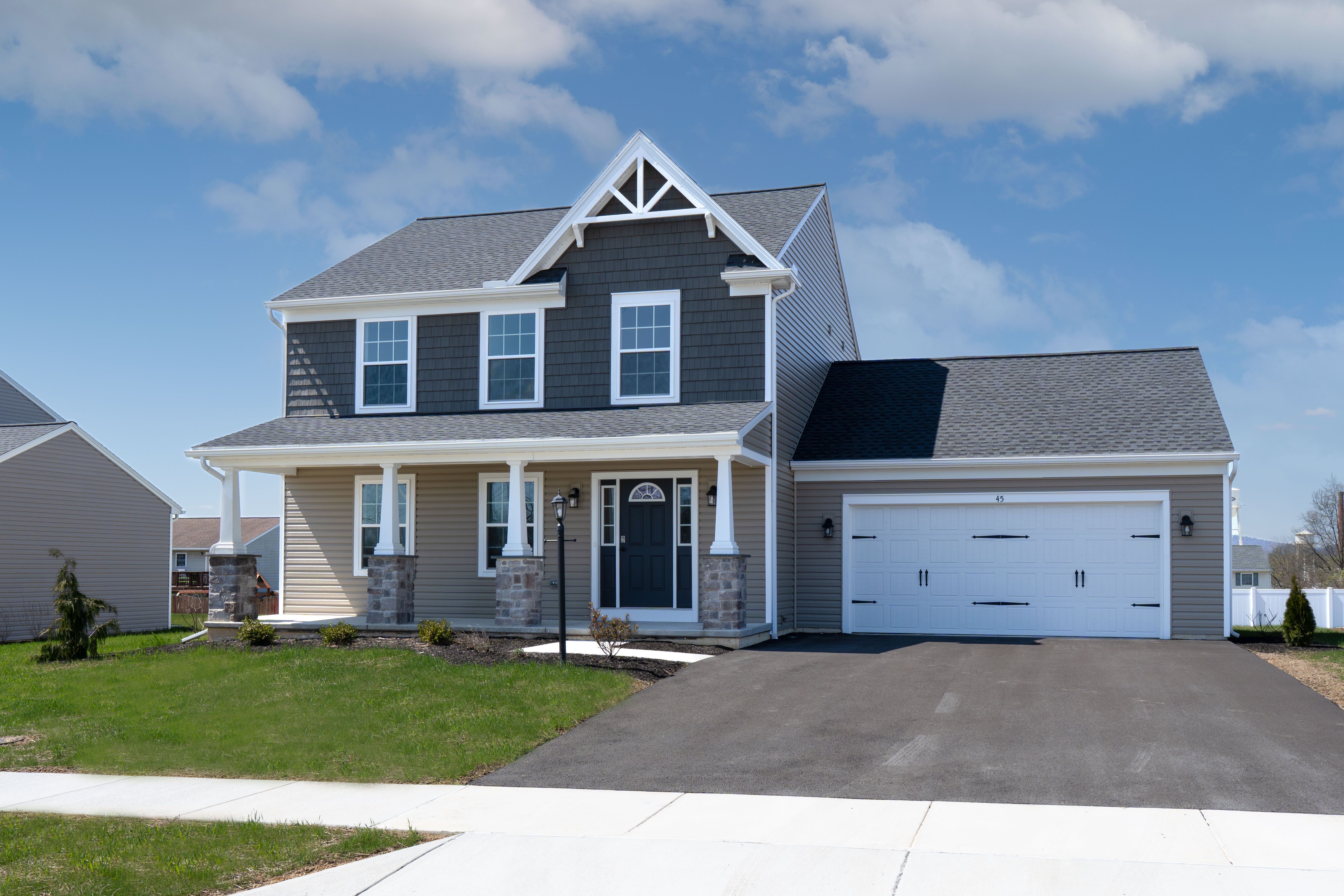 Front view of a two-story home with a gray and tan exterior, stone-accented porch columns, white trim, and a two-car garage.