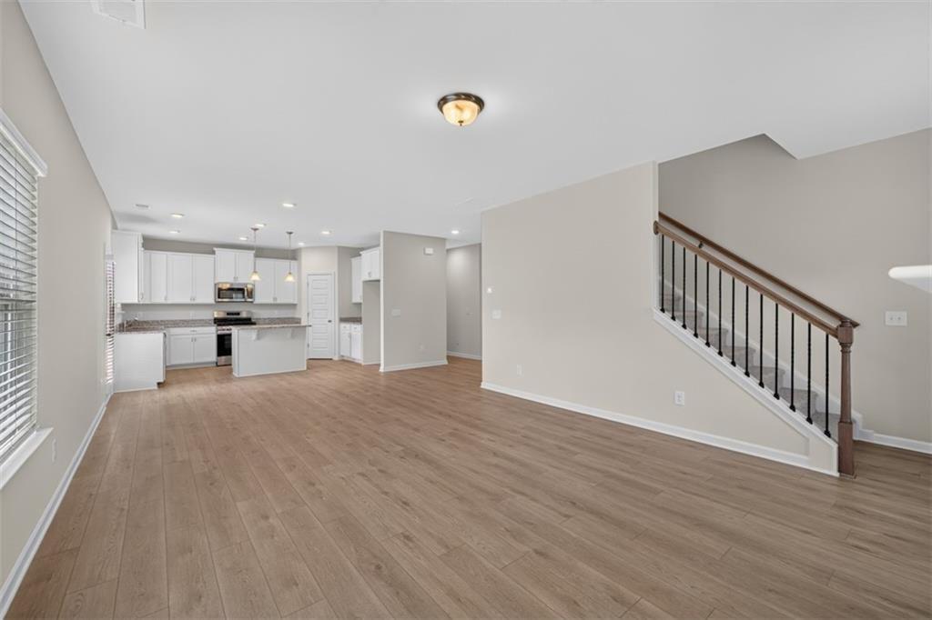 Open-concept living area featuring wood-finish flooring, a white kitchen with stainless steel appli