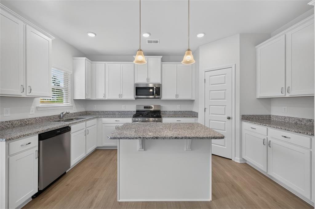 Spacious kitchen featuring an island, light wood-finish flooring, white cabinetry, speckled counter
