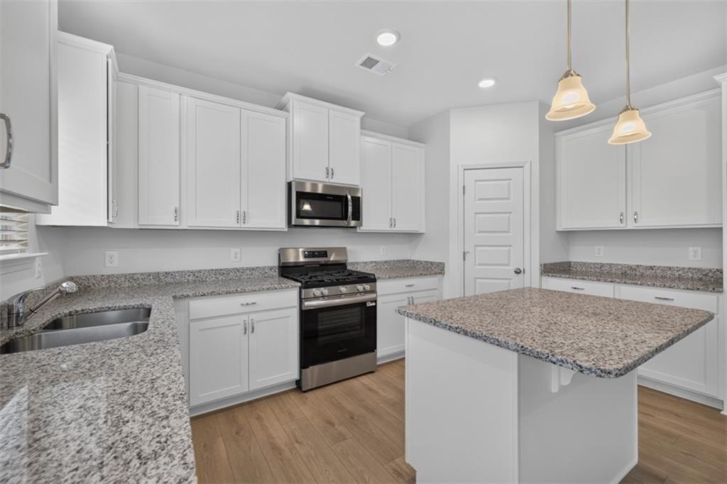 Contemporary kitchen featuring white cabinetry, granite countertops, stainless steel appliances, wo