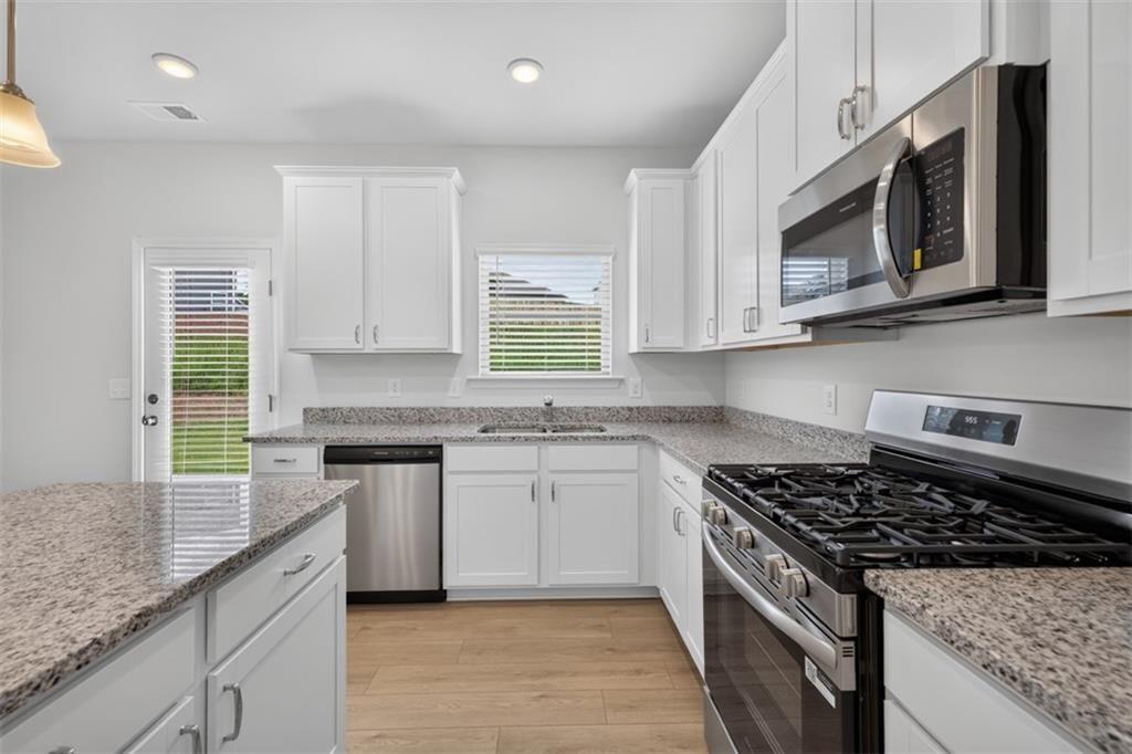 Modern kitchen featuring white cabinetry, granite countertops, wood-finish flooring, stainless stee