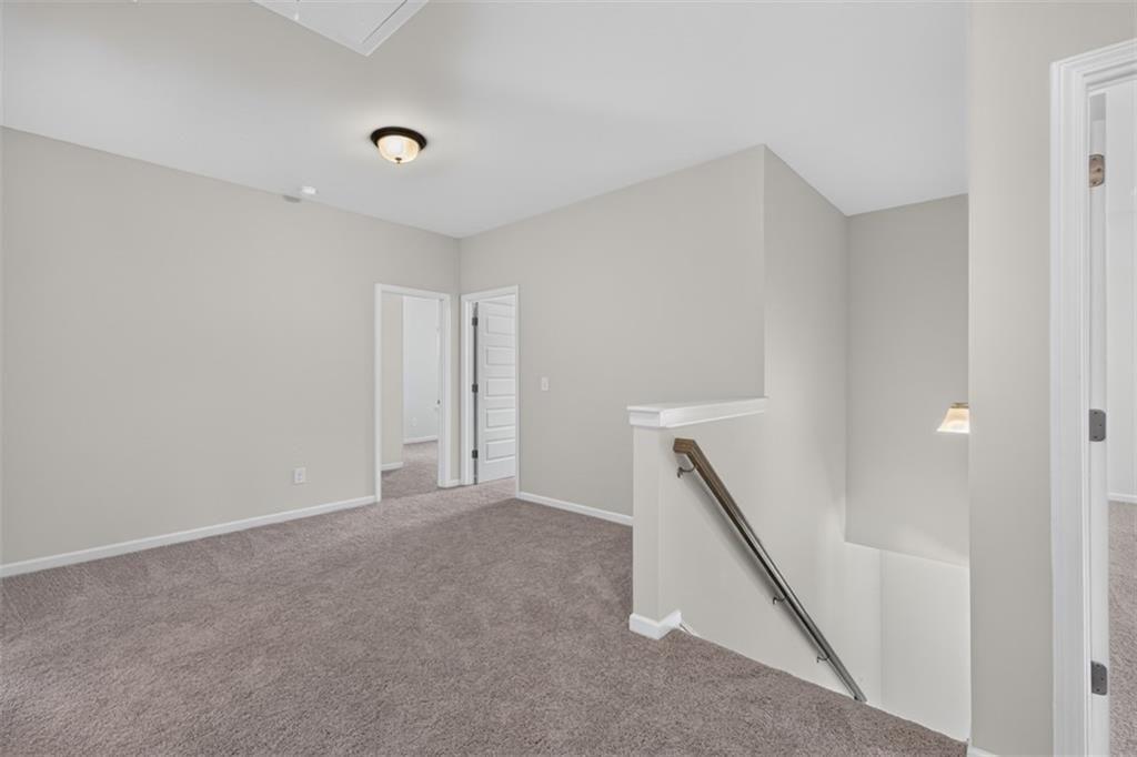 Carpeted landing featuring a half-wall balustrade with a metal handrail, recessed wall sconce, and