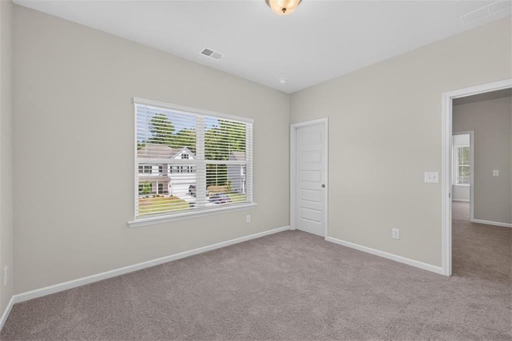 Carpeted room featuring a large window with blinds, light gray wall paint, white trim, and a flush