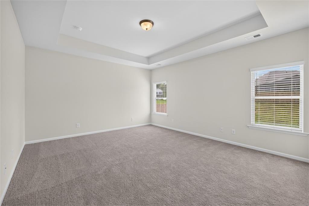 Spacious room featuring neutral paint, gray carpet, a tray ceiling, and two windows with blinds