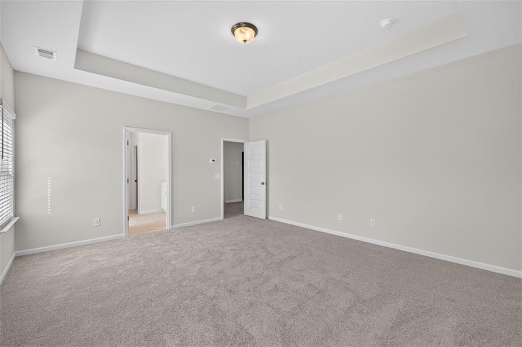 Spacious room featuring tray ceilings, neutral wall paint, and gray carpet flooring