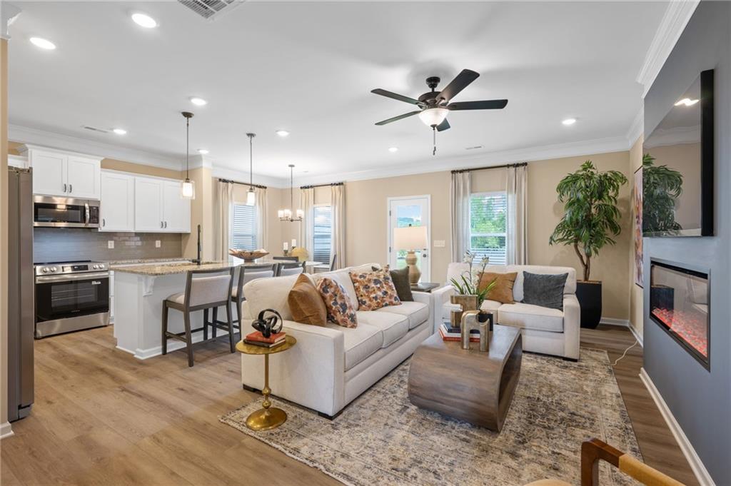 Open-concept living space featuring wood-finish flooring, recessed lighting, a modern ceiling fan, a built-in electric fireplace, and a kitchen island with seating
