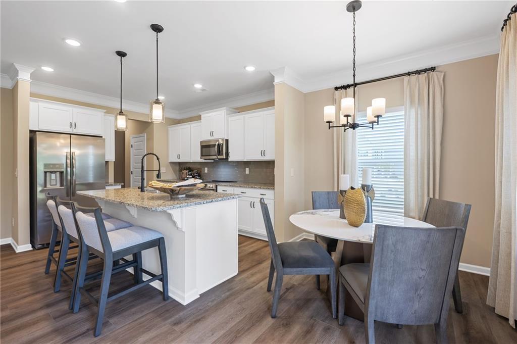 Kitchen featuring an island with stone countertop, stainless steel appliances, white cabinetry, and wood-finish flooring