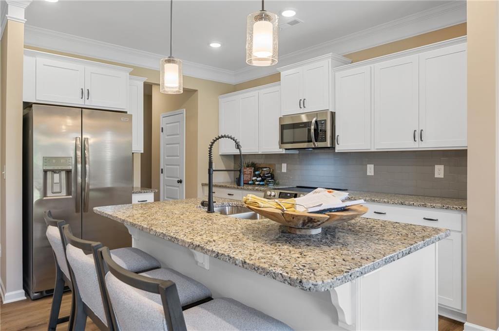 Kitchen featuring white upper and lower cabinetry, stainless steel appliances, speckled countertops, a tile backsplash, and a large island with a built-in sink