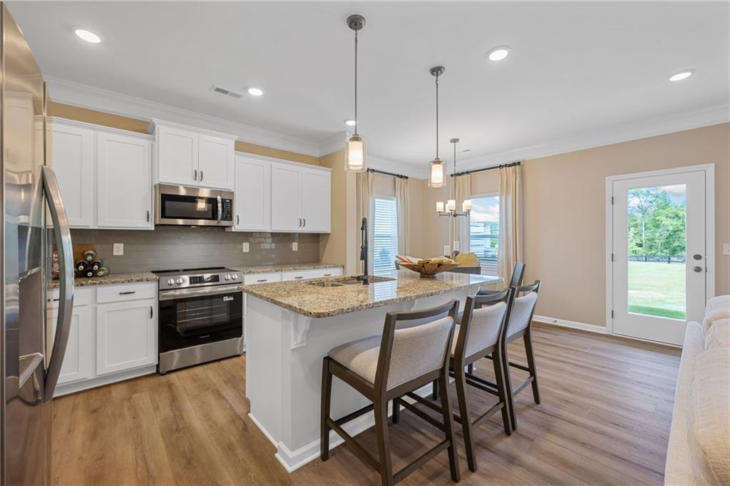 Kitchen featuring white cabinetry, stainless steel appliances, granite countertops, a center island with pendant lighting, and wood-finish flooring