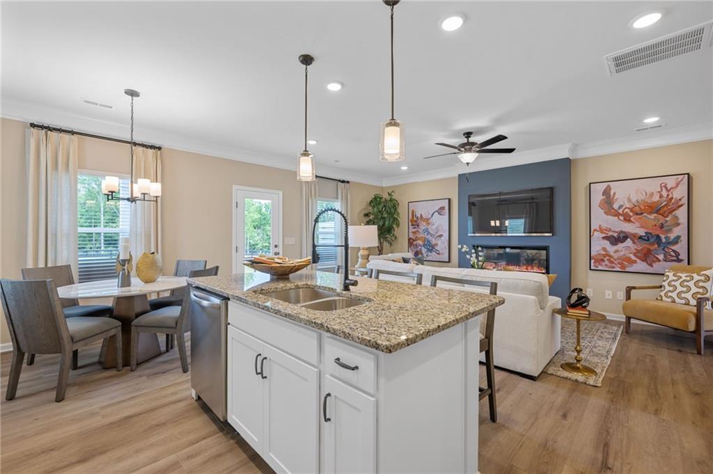 Open-concept living space with wood-finish flooring, a kitchen island featuring a double-basin sink and stone countertop, a built-in electric fireplace, and recessed lighting
