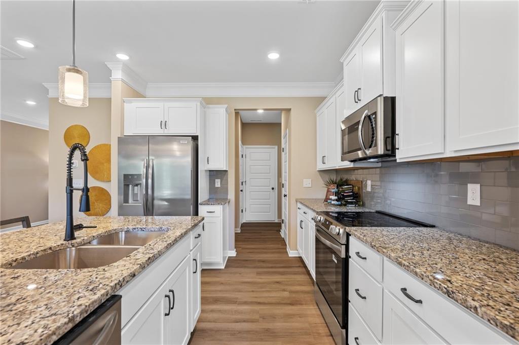 Kitchen featuring white cabinetry, stainless steel appliances, speckled stone countertops, and wood-finish flooring
