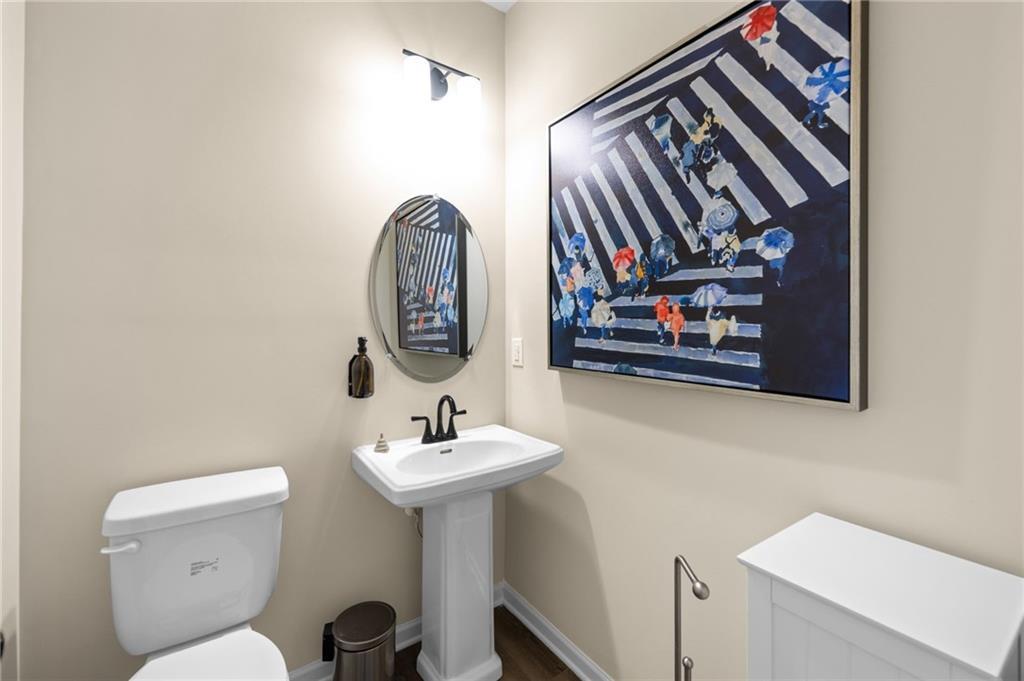 Pedestal sink with a matte black faucet, wall-mounted oval mirror, and wood-finish flooring