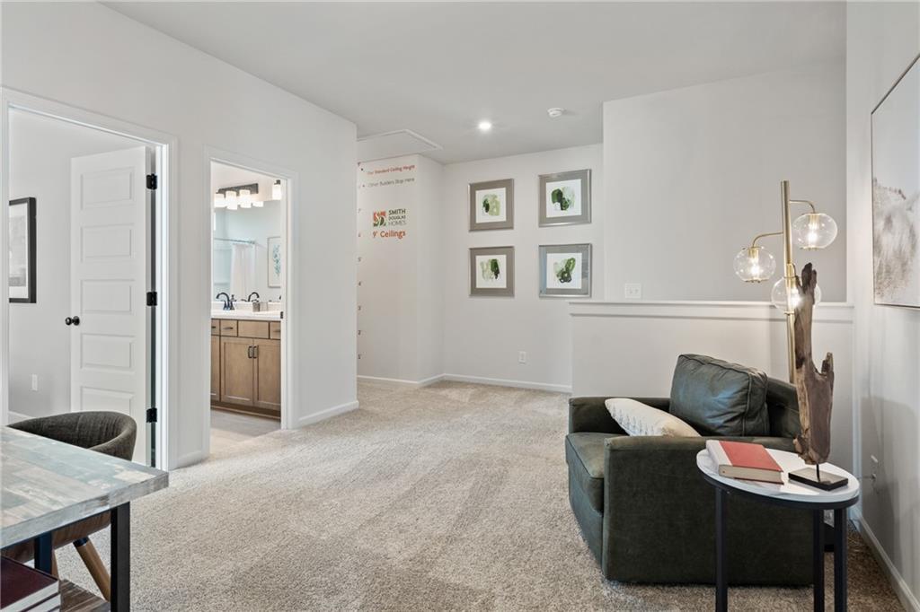 Carpeted loft area with recessed lighting, a half-wall partition, and access to a bathroom featuring a double vanity with a light wood-finish cabinet and wall-mounted lighting