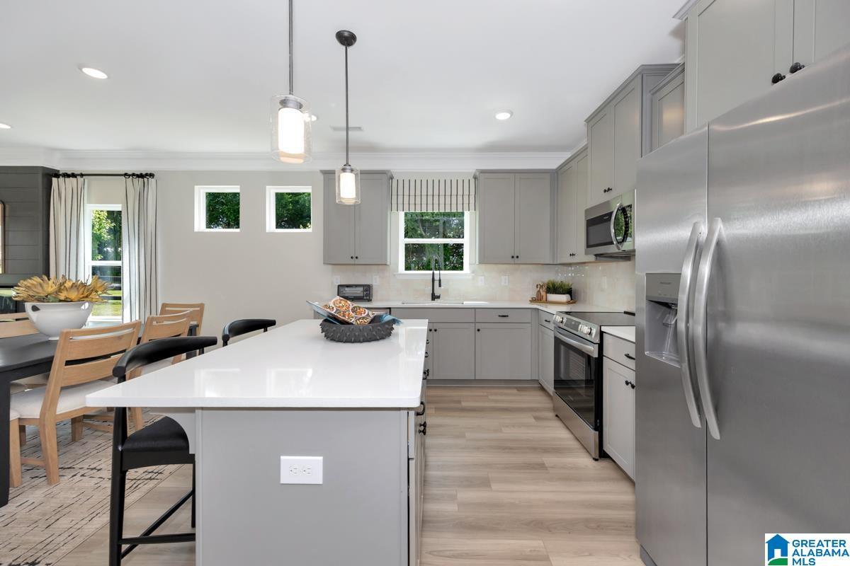 Kitchen featuring a large island with white countertop, light gray cabinetry, stainless steel appliances, and wood-finish flooring