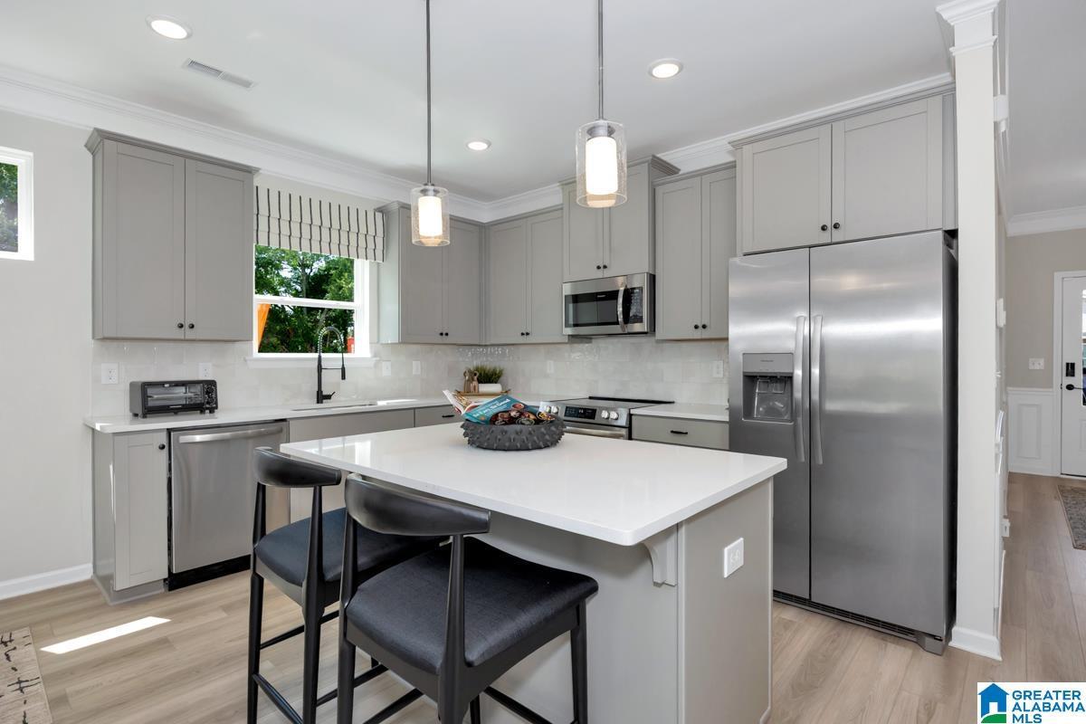 Kitchen featuring light gray cabinetry, stainless steel appliances, a white island with seating, a single basin sink, and wood-finish flooring