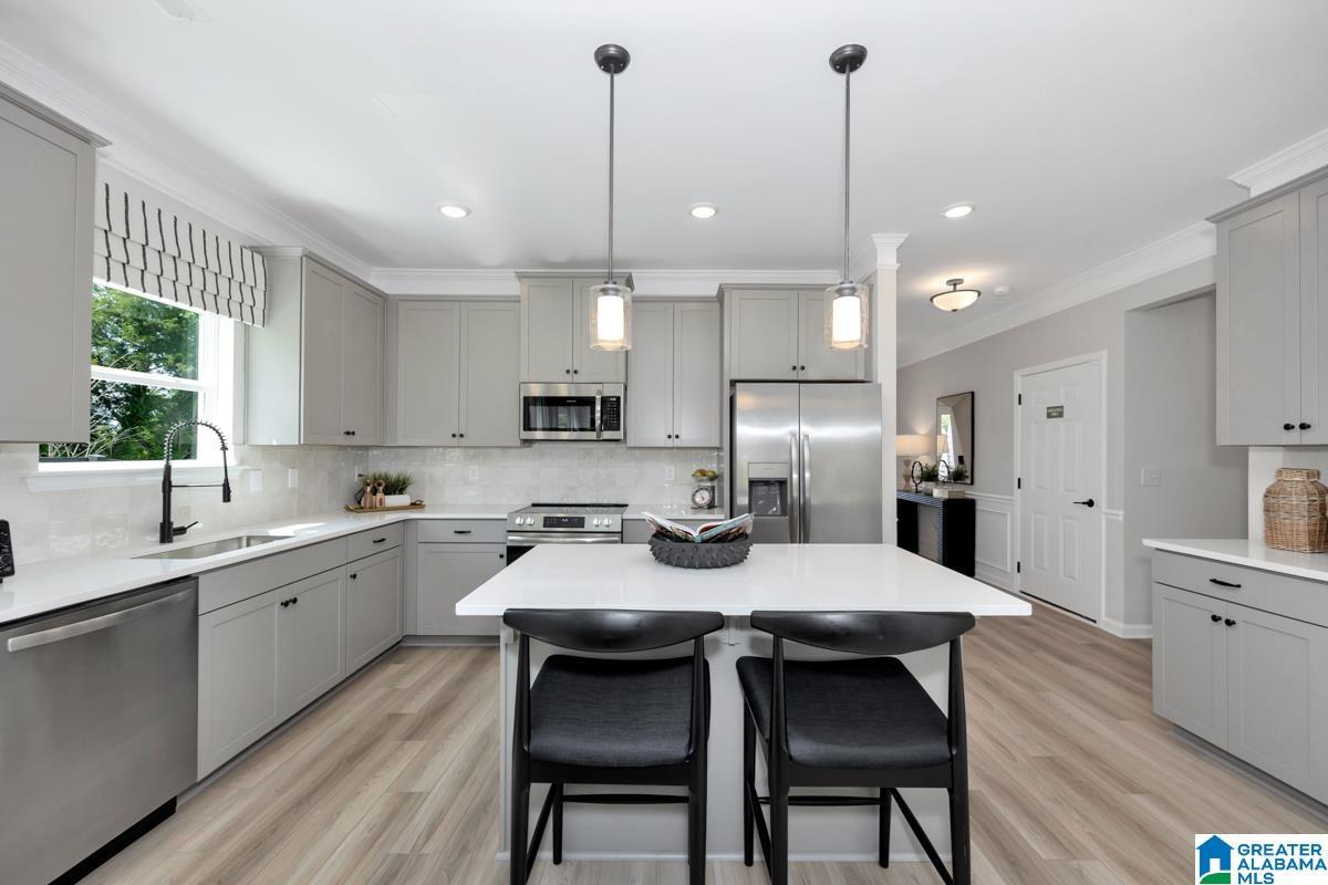 Modern kitchen featuring light gray cabinetry, stainless steel appliances, a center island with counter seating, wood-finish flooring, and pendant lighting