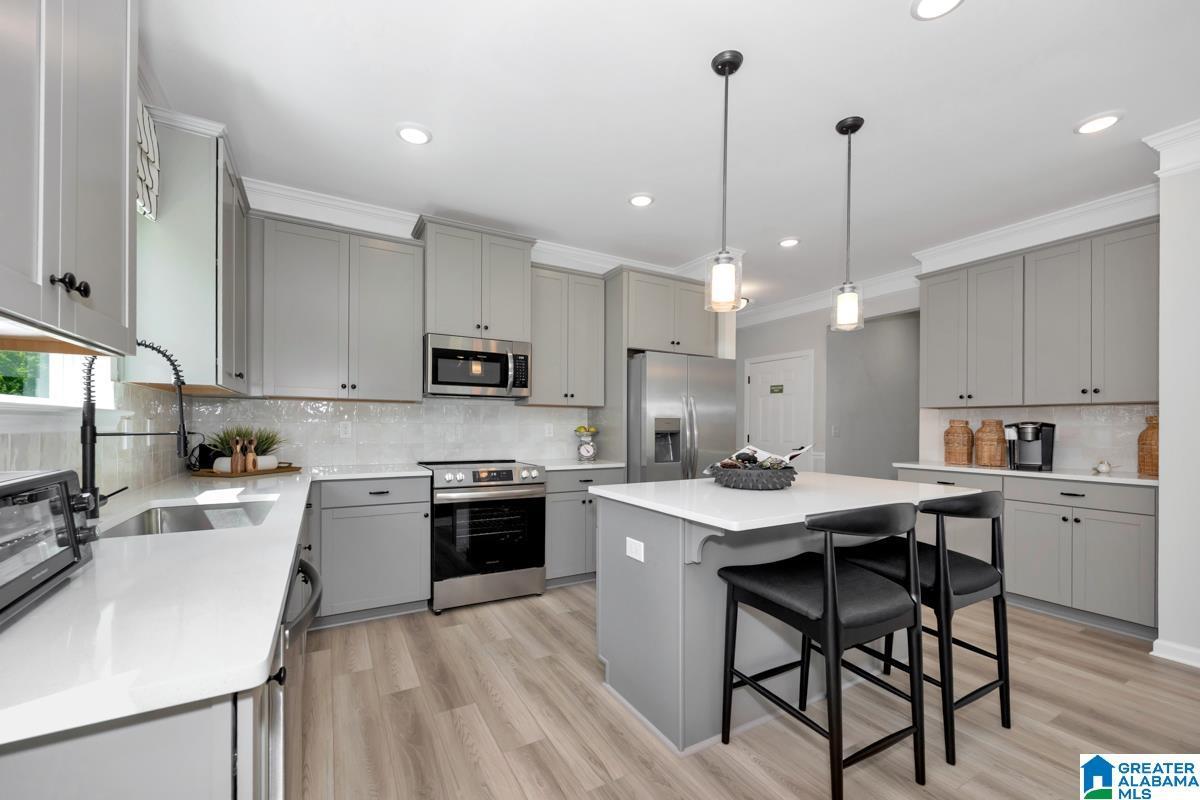 Spacious kitchen featuring light gray cabinetry, stainless steel appliances, a central island with seating, pendant lighting, and wood-finish flooring