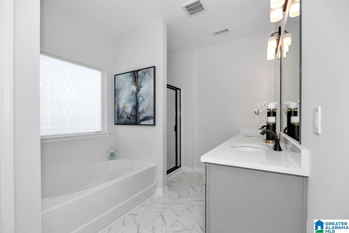 Freestanding soaking tub with privacy window, single vanity with integrated sink, quartz countertop, and patterned tile flooring