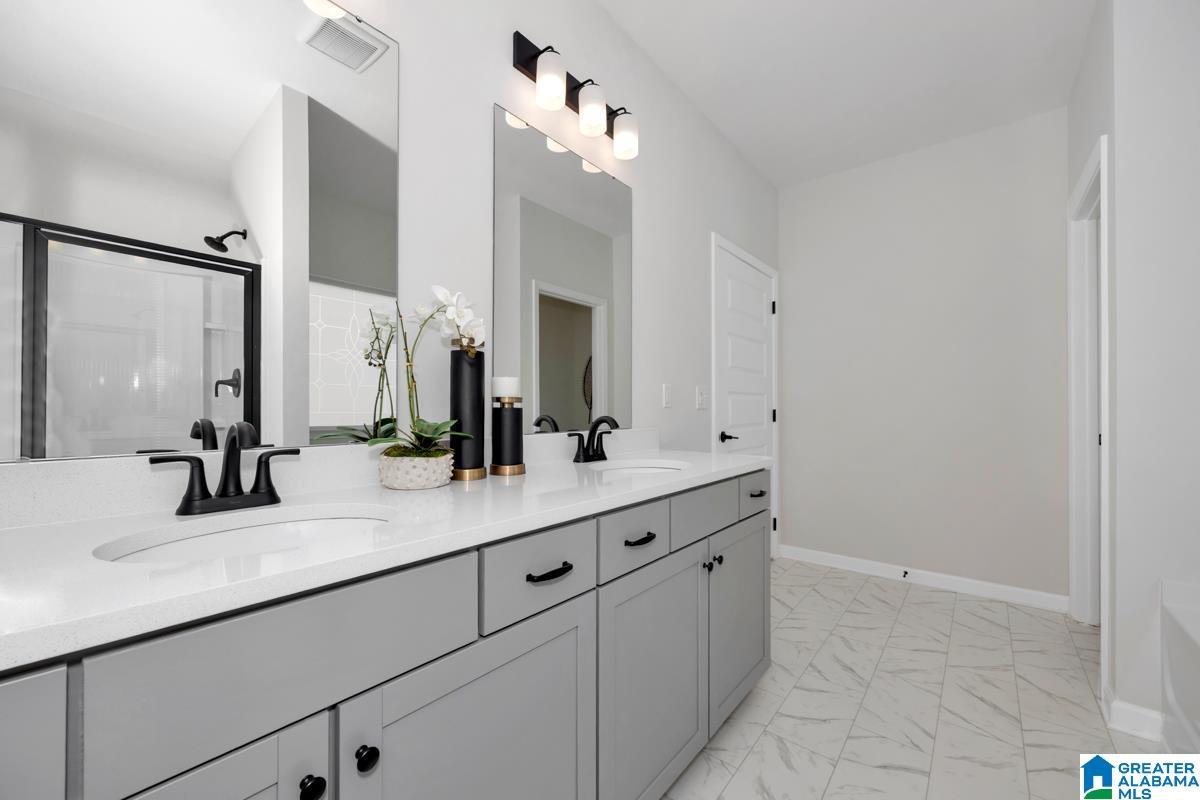 Dual vanity with integrated sinks, light gray cabinetry, matte black fixtures, and a glass-enclosed shower