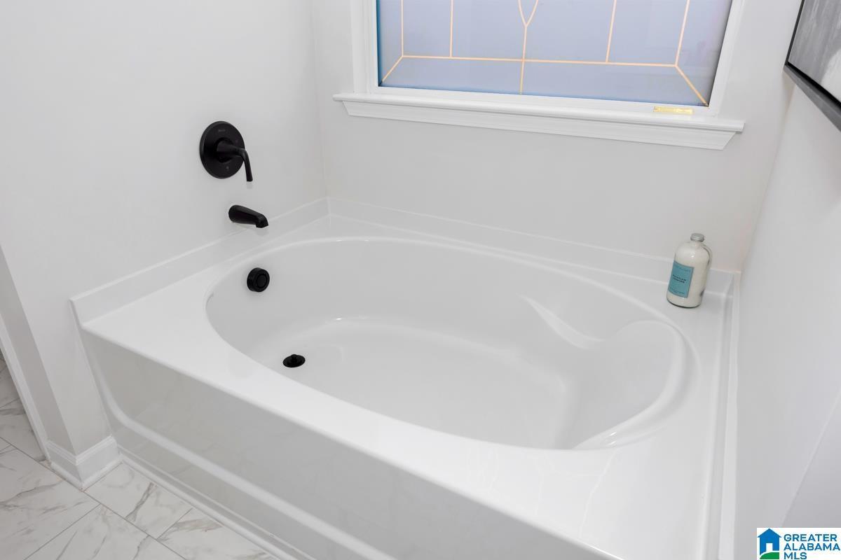 White drop-in bathtub with black fixtures, featuring a built-in window and tiled flooring