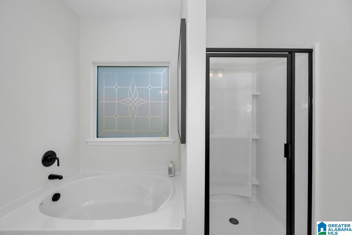 Built-in soaking tub with matte black fixtures, decorative privacy window, and a separate shower enclosure with a dark-framed glass door