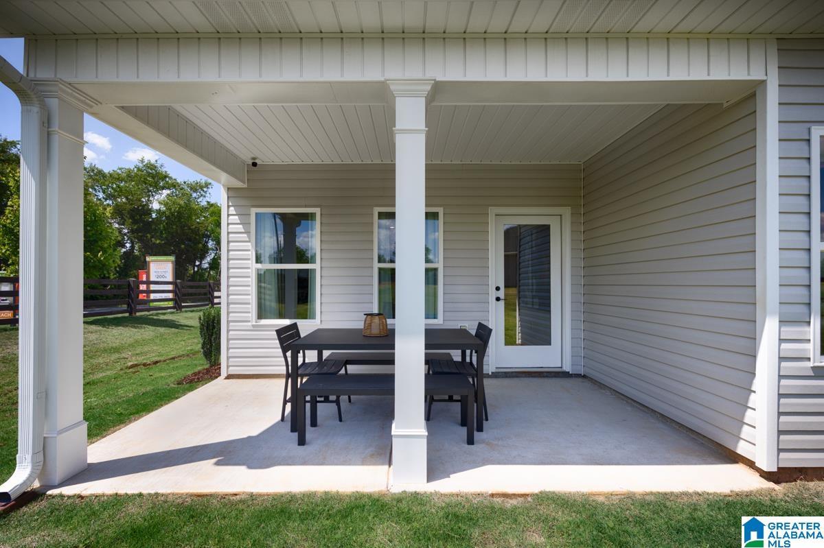 Covered concrete patio with white support columns, light gray siding, and a rear entry door with a full-light panel