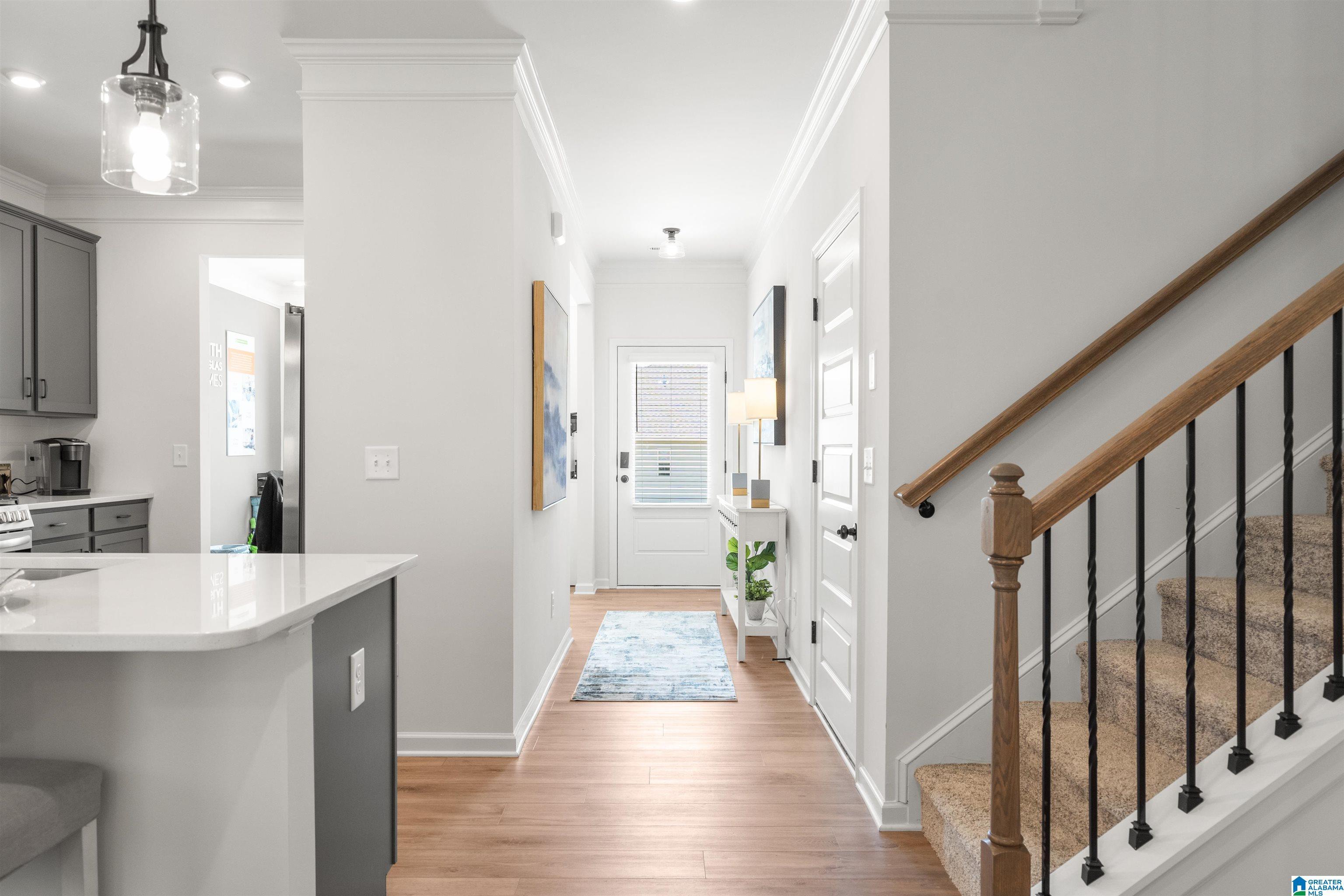 Wood-finish flooring, staircase with wood handrail and wrought iron balusters, white trim and crown molding, recessed lighting, and kitchen island with light-toned countertop