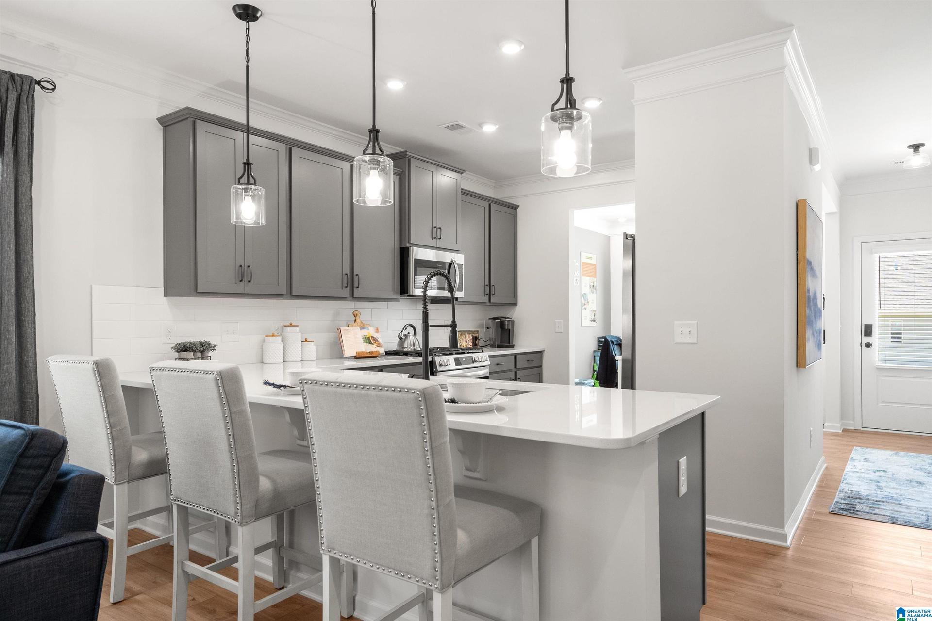 Kitchen featuring gray cabinetry, stainless steel appliances, a white island with seating, pendant lighting, and wood-finish flooring