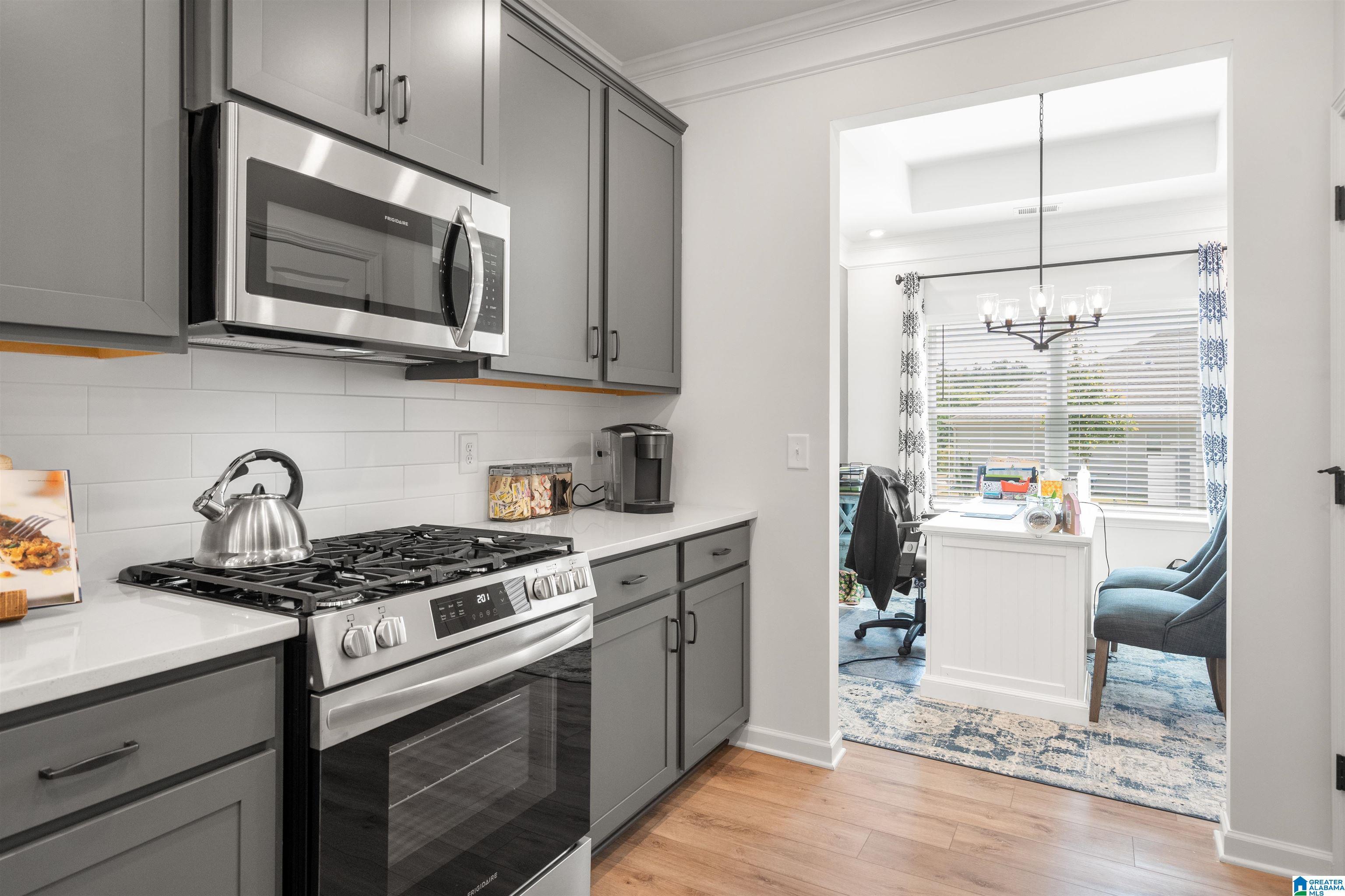 Kitchen featuring stainless steel appliances, grey shaker-style cabinetry, white subway tile backsplash, and light-toned countertops