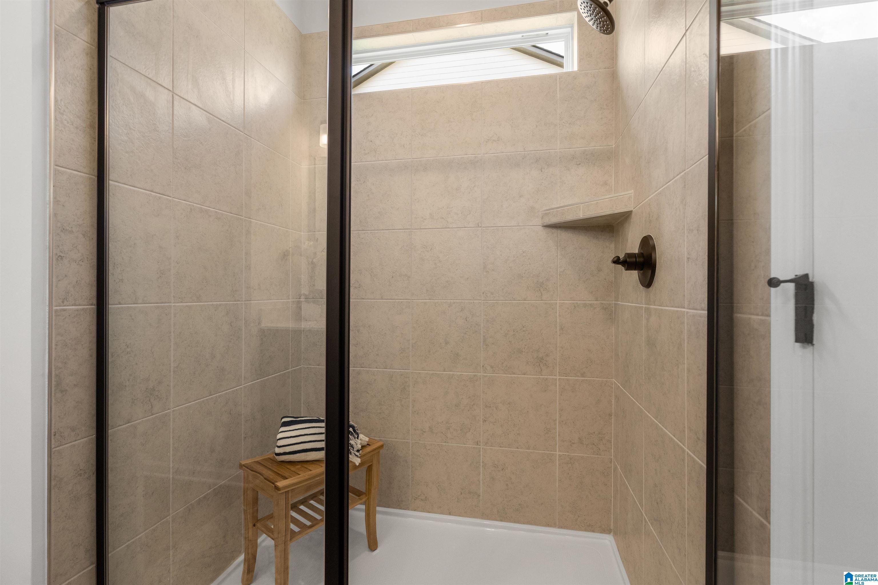 Walk-in shower with neutral tile surround, fixed glass panel, dark-finish hardware, and a built-in shower niche