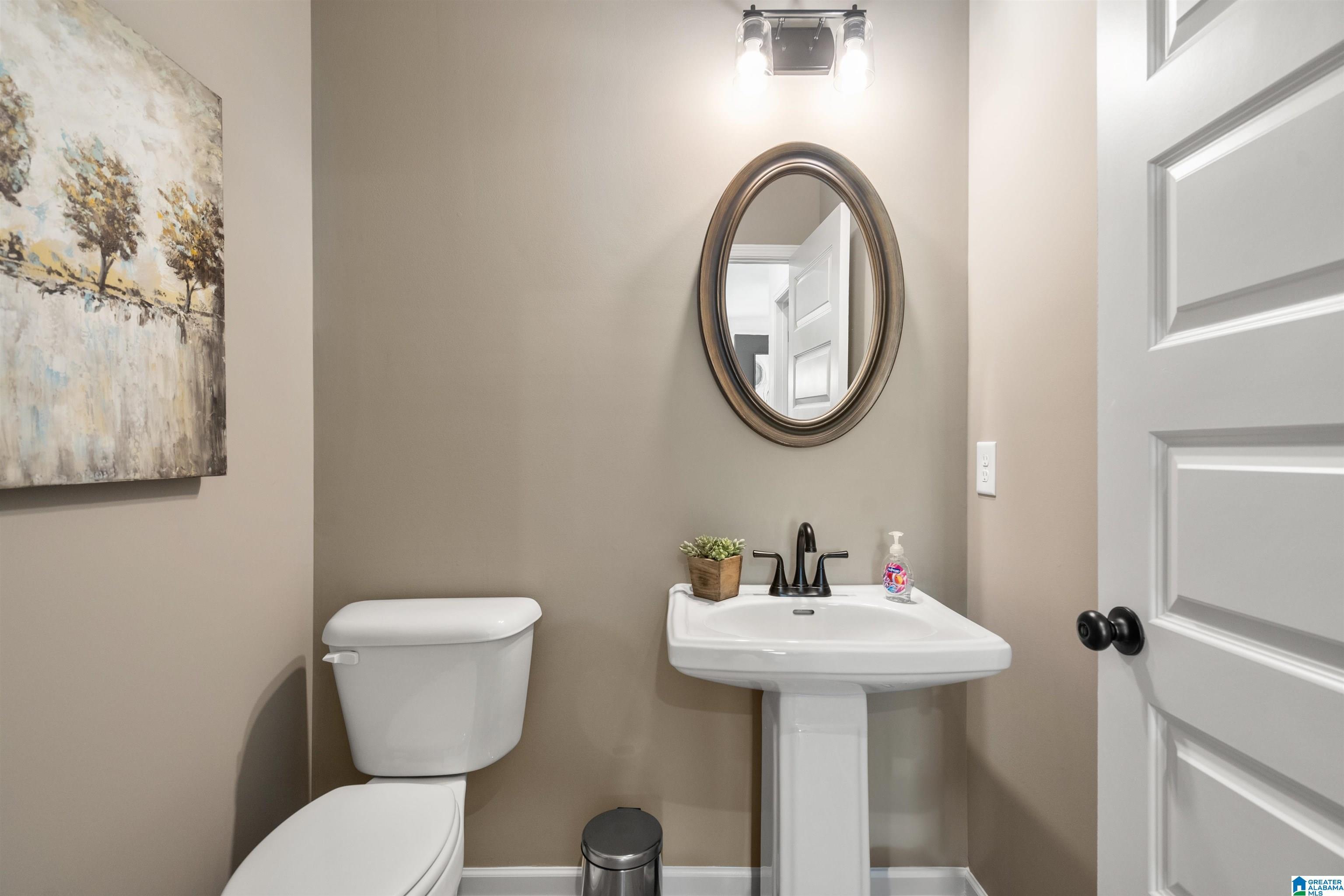 Pedestal sink with a black faucet, oval mirror, and a two-bulb vanity light fixture