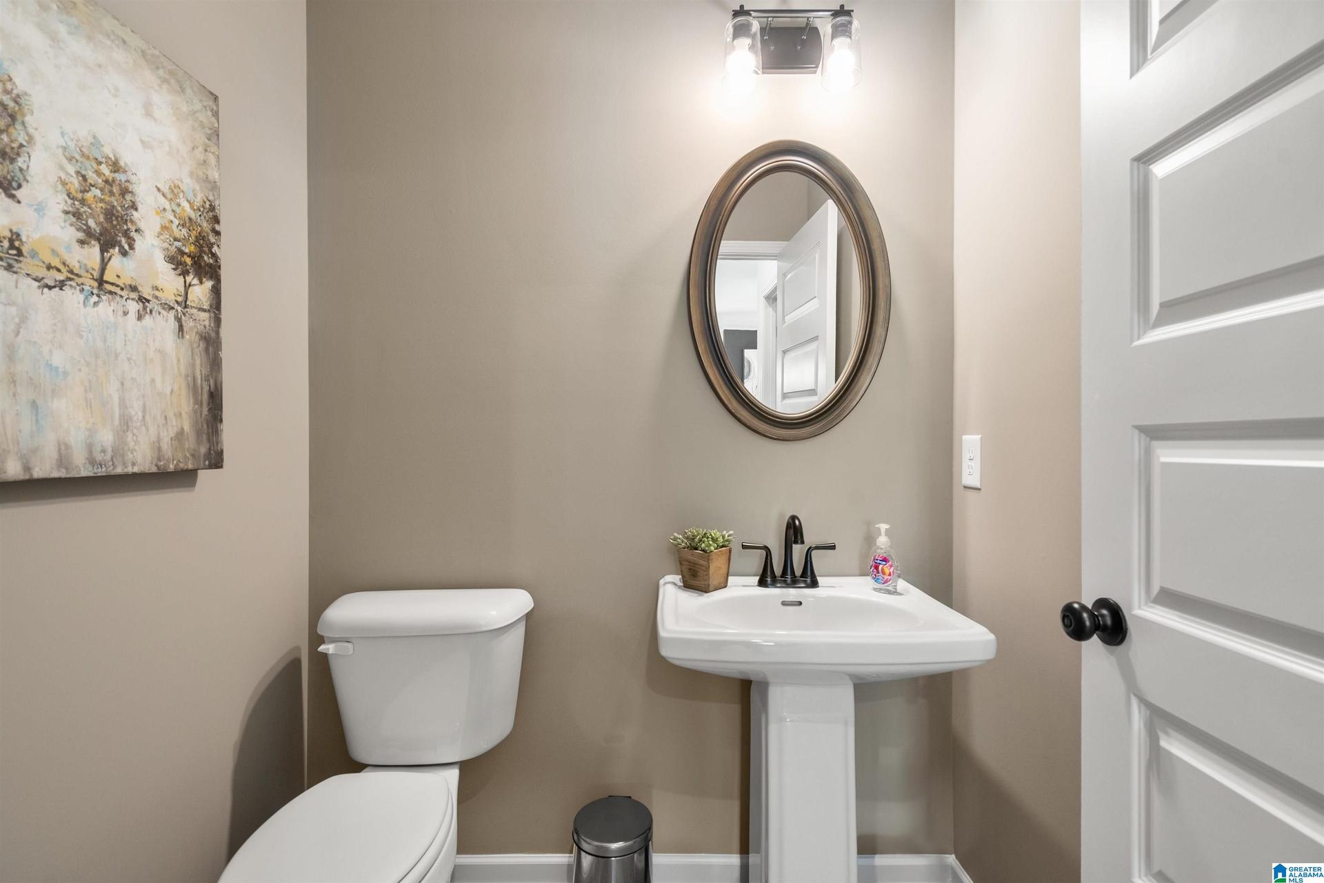 Pedestal sink with a black faucet, oval mirror, and a two-bulb vanity light fixture