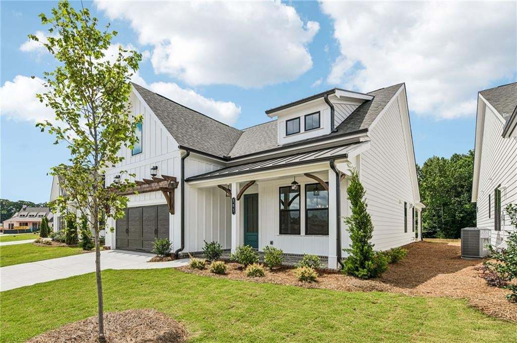 Contemporary farmhouse exterior featuring white board and batten siding, dark-framed windows, a covered front porch with exposed wood accents, a dark metal roof over the porch, and a dormer with black-framed windows