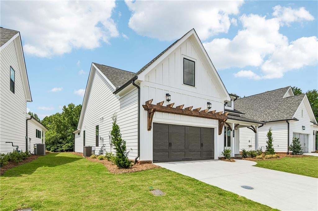 Modern farmhouse exterior featuring white board and batten siding, dark gray garage door, and a decorative wooden pergola with exterior lighting