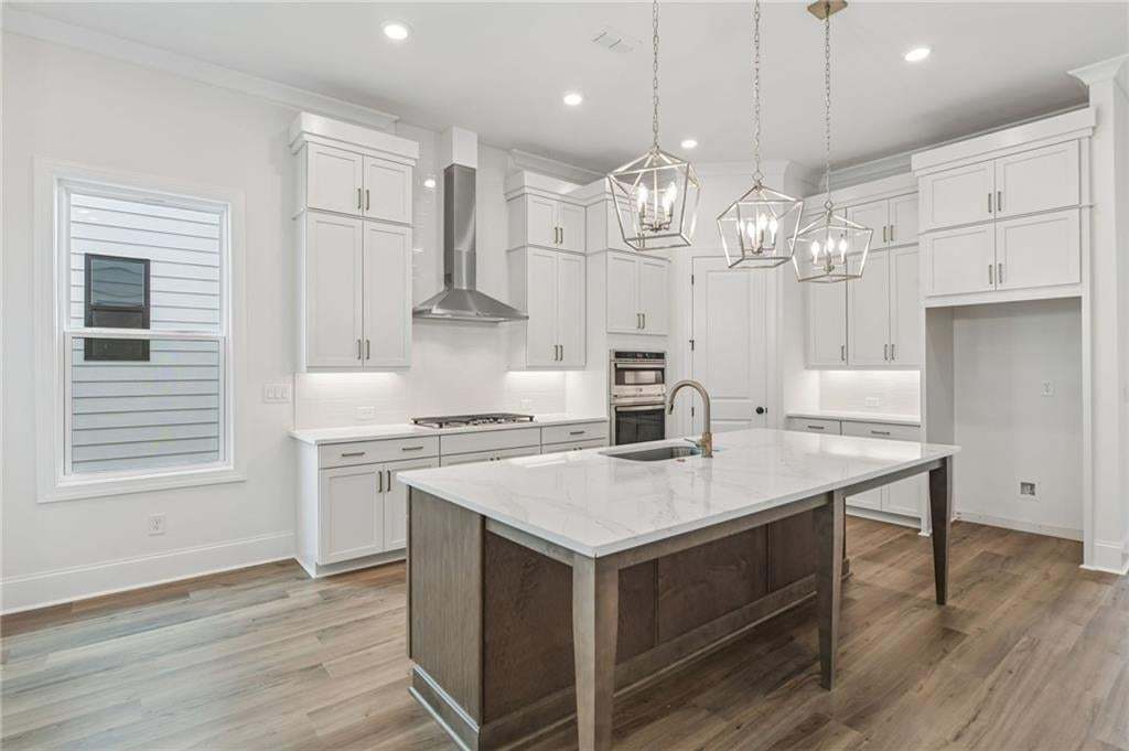 Kitchen featuring a large island with a countertop, recessed lighting, wood-finish flooring, white cabinetry, and stainless steel appliances