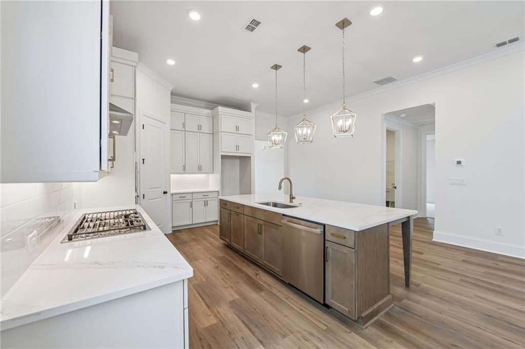 Modern kitchen featuring a gas cooktop, white perimeter cabinetry, a large center island with a sink and stainless steel appliances, and wood-finish flooring
