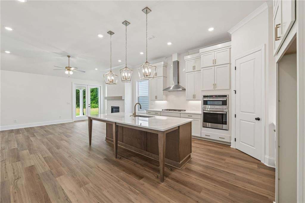 Open-concept living space featuring wood-finish flooring, a kitchen island with stone countertop, stainless steel appliances, white cabinetry, and a fireplace with a mantel
