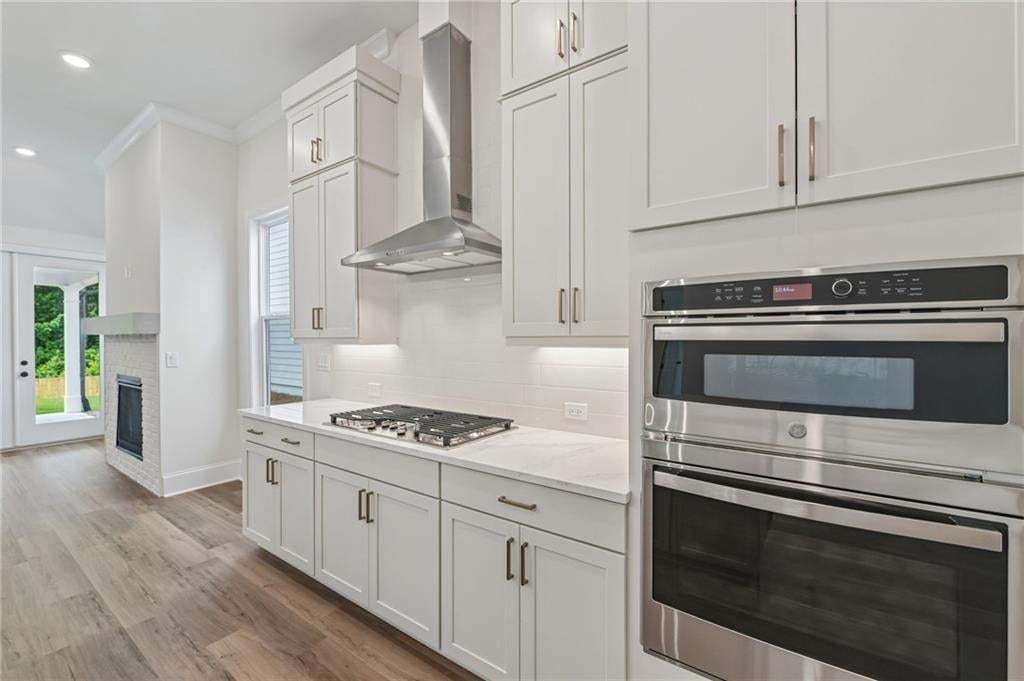 Modern kitchen featuring white cabinetry, stainless steel appliances, a gas cooktop with a range hood, light countertops, and wood-finish flooring